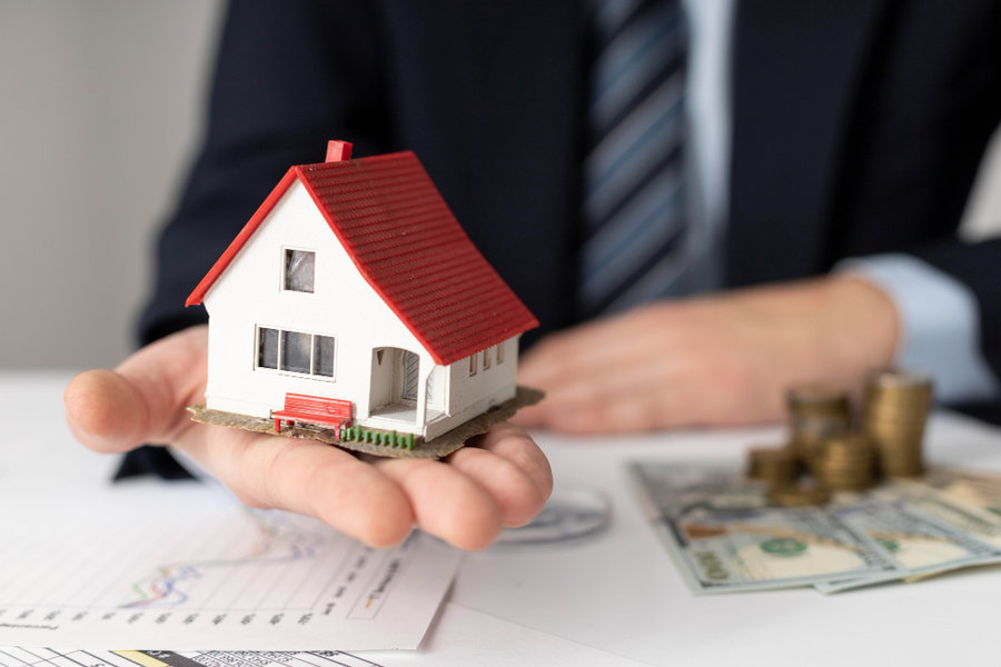 Hand holding a model house over coins and cash